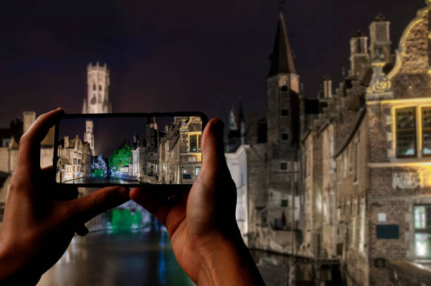 turista tomando fotos del casco antiguo de brujas con sus edificios históricos y canales y torre de campanario por la noche, brujas, bélgica - bruges town hall fotografías e imágenes de stock