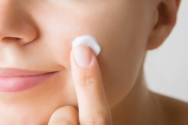 Young adult woman finger applying white moisturizing cream on cheek. Care about clean and soft face skin. Daily beauty product. Closeup. Front view. Young adult woman finger applying white moisturizing cream on cheek. Care about clean and soft face skin. Daily beauty product. Closeup. Front view. cheek stock pictures, royalty-free photos & images