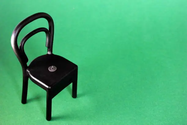 A pushpin on the black plastic chair. Copy space. Green background.