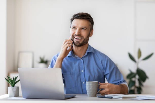 istock Cheerful male entrepreneur talking on mobile phone and drinking coffee in office 1281643184