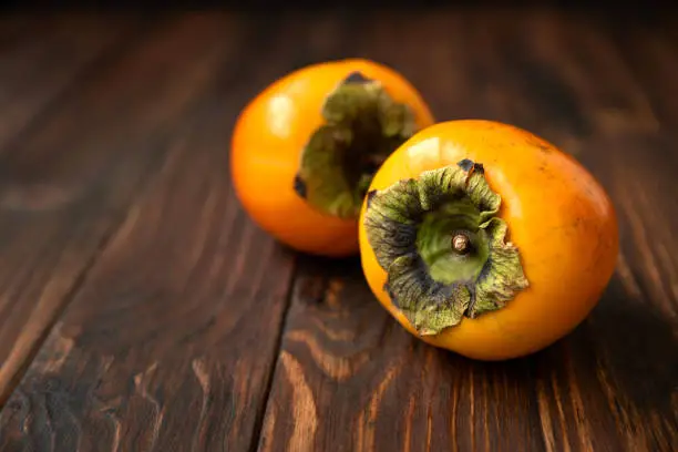 Ripe orange persimmon fruits on wooden background. Selective focus