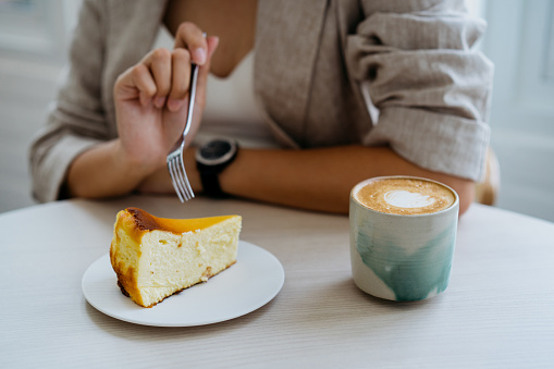 An Asian Chinese woman having cafe latte and cheesecake on top of table