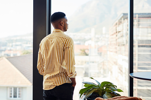 Shot of a young businessman looking thoughtfully out of a window in a modern office