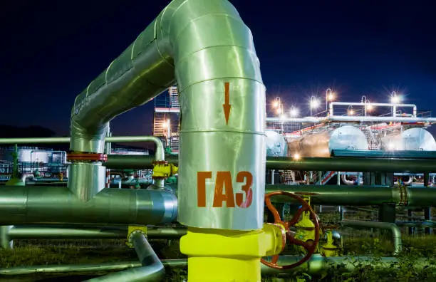 Pipe bend at the oil refinery at night. The word "GAZ" is written on the pipe in Russian. Oil and gas industry