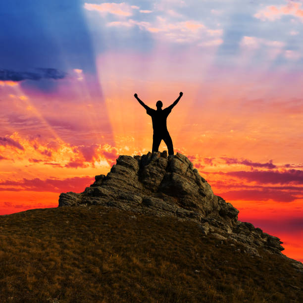 istock man silhouette stay on a mount top at the dramatic sunset, happy winner scene 1281659557