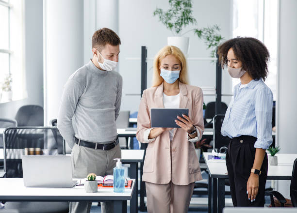istock New task, social distancing and office work after lockdown. Young business woman with protective mask gives tasks to european guy and african american lady in office interior 1281660286
