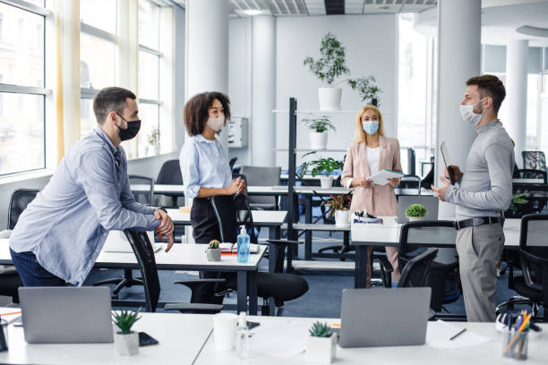 istock Modern team meeting, group work and social distancing. Manager with tablet speaks with workers in protective masks in interior of modern office with gadgets 1281660474