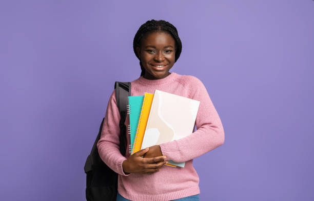 istock Smiling black female student with workbooks and backpack posing on purple background 1281661140