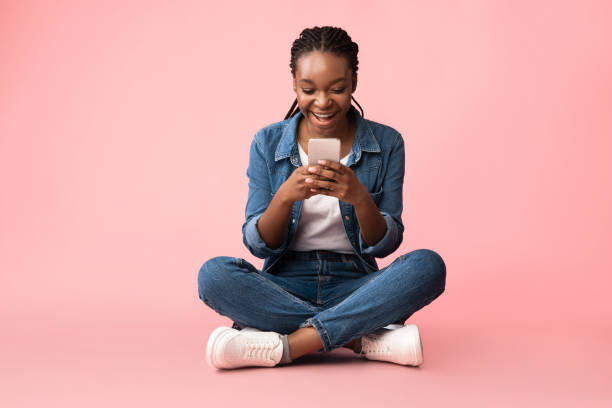 istock Excited African Lady With Cellphone Texting Sitting Over Pink Background 1281661297