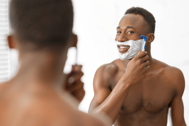 istock Cheerful Black Guy Shaving Face Standing Near Mirror In Bathroom 1281661325