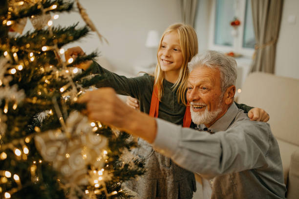 Senior man and granddaughter decorate christmas tree stock photo