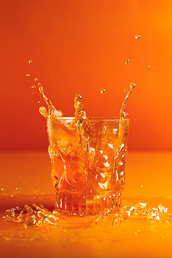 Splash of orange liquid in transparent glass cut glass on orange background