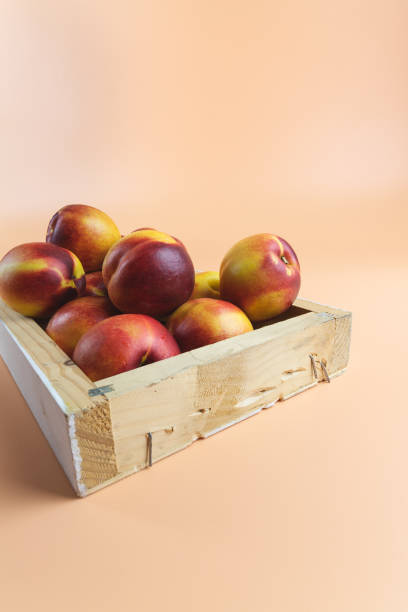 Red very ripe peaches, nectarines inside a wooden box for sale. Peachy colored background