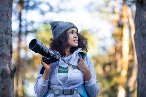 African American woman walking in the forest with a camera looking by side. Close up photo.
