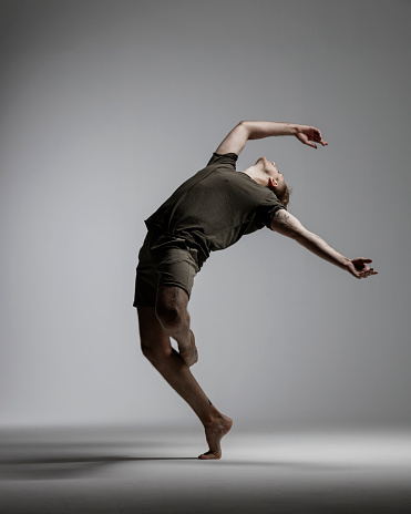 Full length shot of a ballerina dancing and leaning backwards isolated on gray background