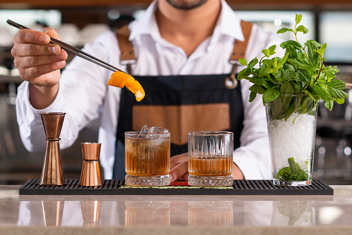 Male bartender adding lemon peel in a drink with tongs