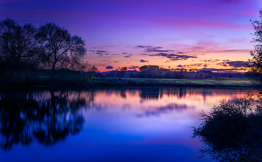 Vibrant sky at dusk as sun sets over the Rive Wye at Glasbury, Powys, Wales. Brecon Beacons in background. Autumn scene.