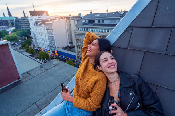 Two beautiful girls celebrate, toasting their friendship Happy girlfriends drinks beer and enjoy laughing at rooftop woman drinking beer stock pictures, royalty-free photos & images