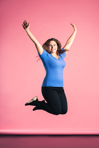 Plus size model in casual clothes jumping in studio on pink background, body positive concept