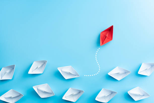 Group of white paper ship in one direction and one red paper ship pointing in different way on blue background. Business for innovative solution concept.