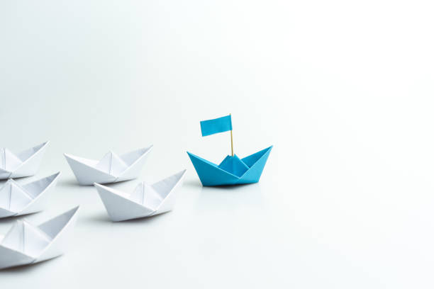 leadership concept, blue paper ship leading among white on white background. - forward fold imagens e fotografias de stock