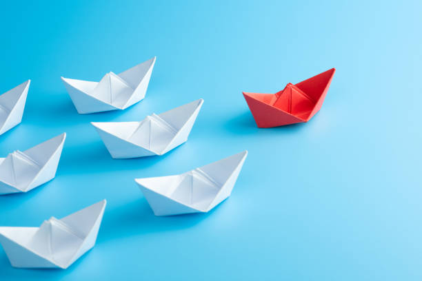 Leadership concept. Red leader paper ship leading among white on blue background. stock photo