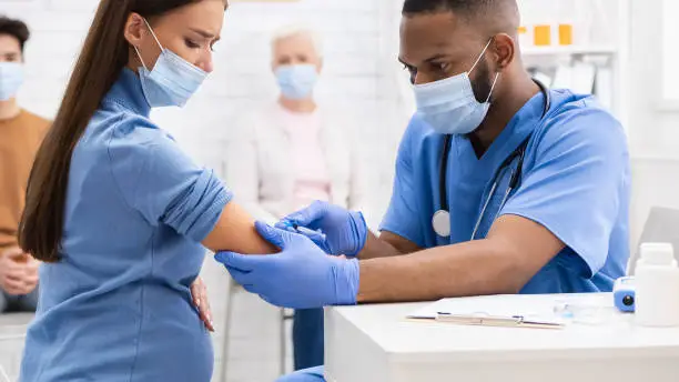 Photo of Pregnant Lady In Mask Receiving Coronavirus Vaccine Injection In Hospital