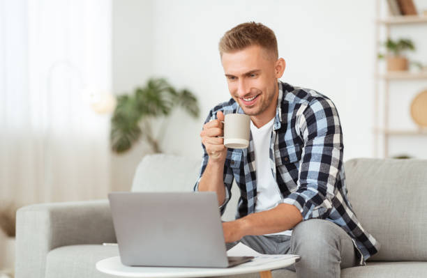 istock Portrait of man sitting on couch with coffee using laptop 1281675919