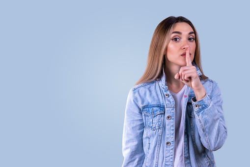 A young girl in a blue denim jacket puts her finger to her lips. A sign of silence. Don't talk.