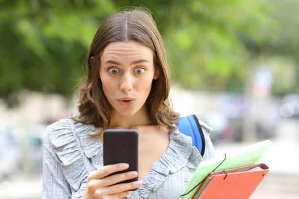 Surprised student checking phone in the street