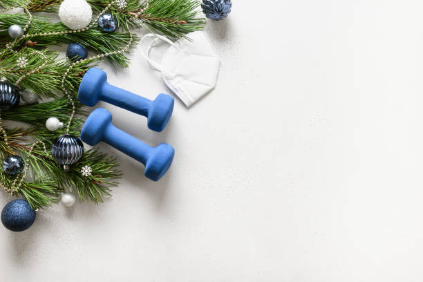 istock Christmas composition with blue dumbbells, medical mask, and gift on white. 1281680728