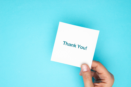 Woman holding thank you card in front of a blue background.