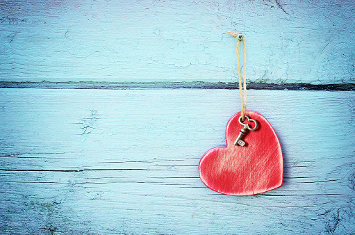 Bronze key and red wooden heart hanging on antique teal blue old wood door. Valentines Day. Holiday concept.
