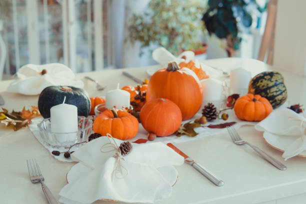 istock Festive table setting for Thanksgiving family home dinner. Fall composition with decorative pumpkins, nuts, cones, fallen leaves, and candles in light interior. Natural autumn decor. Selective focus 1281685546