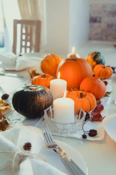 istock Festive table setting for Thanksgiving family home dinner. Fall composition with decorative pumpkins, nuts, cones, fallen leaves, and candles in light interior. Natural autumn decor. Selective focus 1281685558