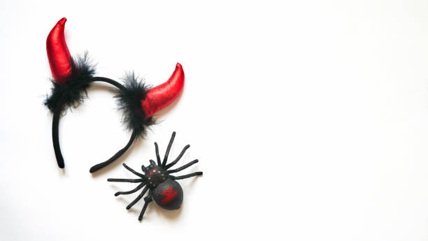 istock Red devil horns head hoop and plastic toy insect black spider on white background. Accessory for Halloween celebration, top view, flat lay, copy space 1281685916