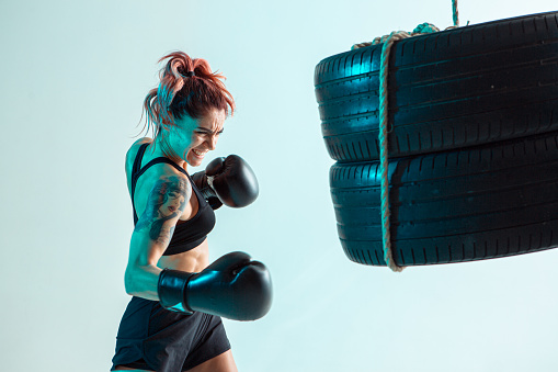 A female fighter in Boxing gloves strikes the tires with her hand. High quality photo