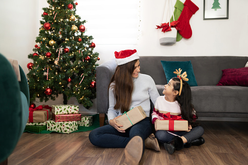 Portrait of a cute mother and daughter exchanging Christmas presents while sitting next to the tree at home