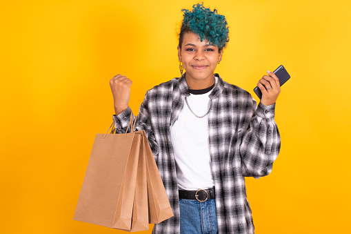 young girl with mobile phone and shopping bags isolated on yellow background