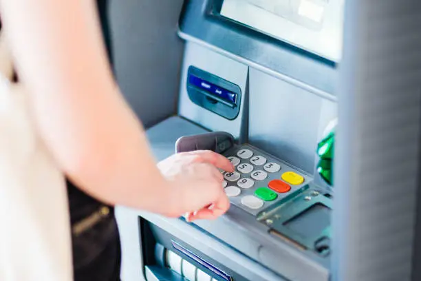 Closeup of a caucasian adult person pressing on ATM machine keypad number to withdraw cash money.