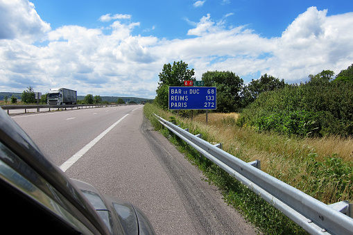A road sign to the towns of Bar le Duc, Reims and Paris, 272 km away, on an abandoned highway among green trees and grass on the wayside. Sunny day. Copy space.