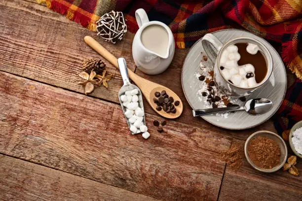 This is a photograph of hot chocolate on a wood background surrouned by ingredients