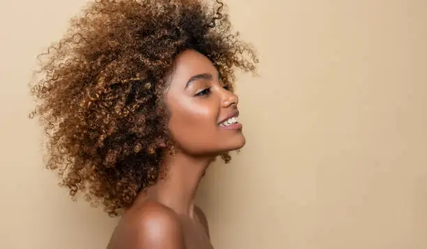 Expression of happiness and pleasure on the face of  dark skinned young woman. Natural, dense afro hair on the head of young beautiful model, white toothy smile on her face. Girl with vibrant, melanin-rich skin tone.