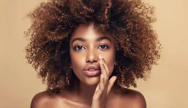 Photo of Young brown skinned woman is sharing new secrets with Us. Natural, dense afro hair on the head of young beautiful model.