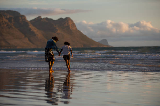 istock Rear view Sister's reflection at the beach with mountain backdrop holding hands 1281700104