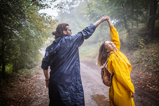 Photo of happy love couple in raincoats dancing on the rain in a forest.