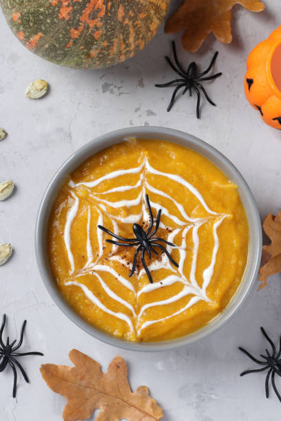 Halloween pumpkin soup with creamy spider web in gray bowl and spiders on the table. View from above. stock photo
