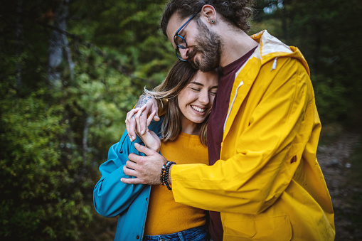 Photo of happy couple in raincoats embracing outdoors on a rain day in forest.