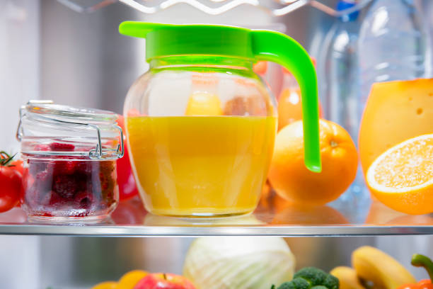 Open refrigerator door. Freshly squeezed orange juice in a jug. Fruit on the shelf of the refrigerator. stock photo