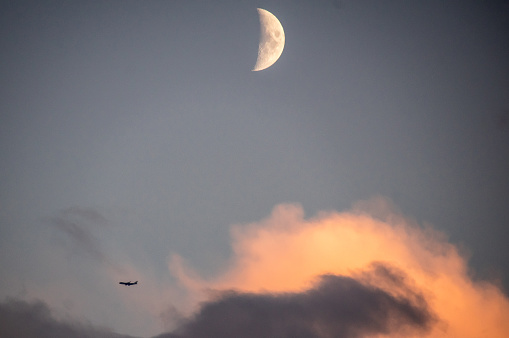 Sun reflection in the clouds with rising moon and passing airplane